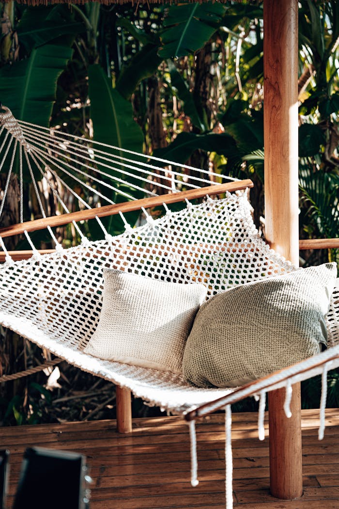 A cozy hammock with pillows in a tropical setting on a wooden verandah surrounded by lush greenery in Tanzania.